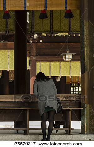Stock Photo - Tokyo, Japan: March 2, 2013 - Young woman seen from behind bowing in traditional manner at Shinto Mehji shrine, Tokyo, Japan. Fotosearch