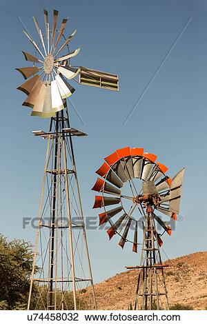Stock Image - Two ranch windpumps of different heights, set at right angles to each other, each with rotary metal blades, one silver, one red, Namib desert, Namibia, South West Africa. Fotosearch