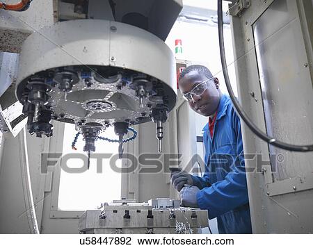 Stock Image - Apprentice engineer using CNC (computer numerical controlled) lathe in factory, portrait. Fotosearch