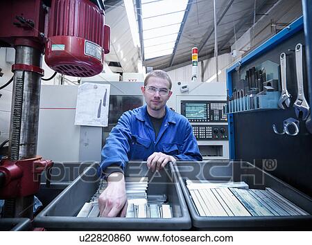 Stock Image - Apprentice engineer with components in factory, portrait. Fotosearch