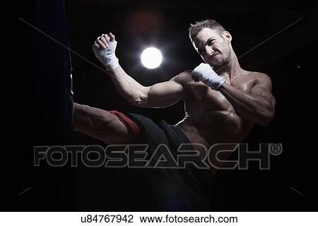Stock Image - Boxer kicking punch bag. Fotosearch