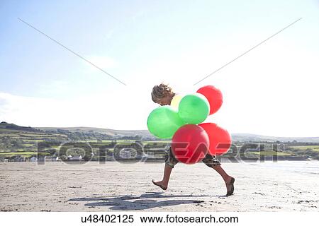 Boy on beach holding balloons, Wales, UK View Large Photo Image Stock Photography - Boy on beach holding balloons, Wales, UK. Fotosearch