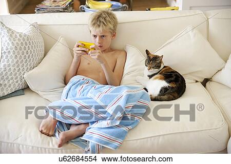 Picture - Boy sitting on sofa playing handheld game. Fotosearch