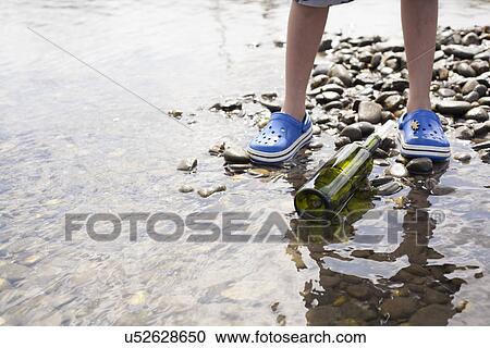 Stock Image - Boy standing by message in a bottle at seaside. Fotosearch