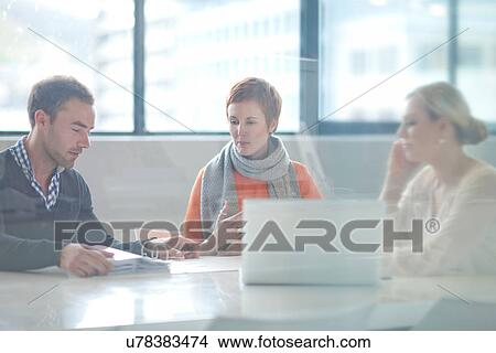 Businesspeople sitting at conference table looking at laptop View Large Photo Image Picture - Businesspeople sitting at conference table looking at laptop. Fotosearch