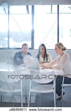 Stock Image - Businesspeople sitting at conference table looking at laptop. Fotosearch