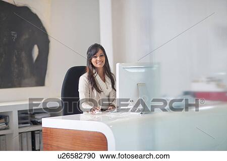 Businesswoman sitting at desk using computer View Large Photo Image Stock Image - Businesswoman sitting at desk using computer. Fotosearch