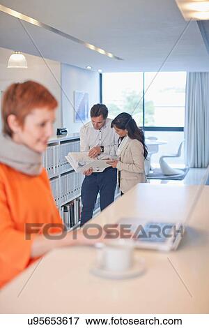 Stock Photo - Businesswoman sitting at table using laptop, colleagues looking at folder in background. Fotosearch