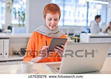 Stock Photograph - Businesswoman sitting at table using digital tablet. Fotosearch