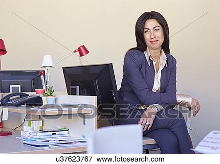 Stock Photo - Businesswoman wearing suit sitting at desk. Fotosearch