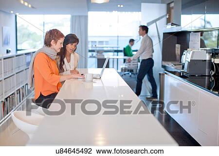Businesswomen sitting at table looking at laptop View Large Photo Image Stock Image - Businesswomen sitting at table looking at laptop. Fotosearch