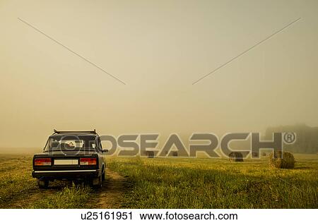 Stock Image - Car driving through field of haystacks on overcast day. Fotosearch