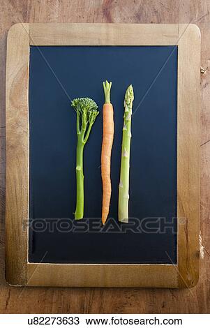 Stock Image - Carrot, brocolli and apsaragus on blackboard, still life. Fotosearch