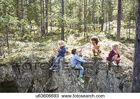Stock Image - Children sitting on rocks in forest eating picnic. Fotosearch