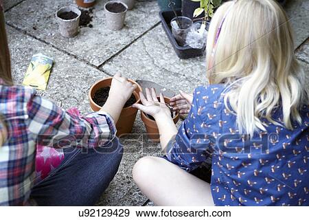 Stock Photo - Close up of two girls in garden planting seeds into pots. Fotosearch