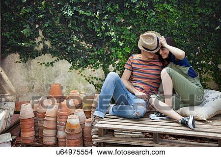 Picture - Couple sitting on wooden palettes, man wearing straw hat. Fotosearch