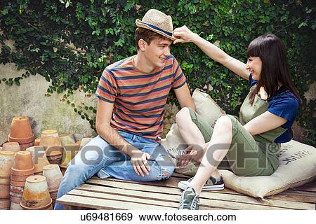 Stock Photo - Couple sitting on wooden palettes, man wearing straw hat. Fotosearch