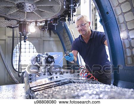 Stock Image - Engineer cleaning computer numerical controlled (CNC) lathe in factory. Fotosearch