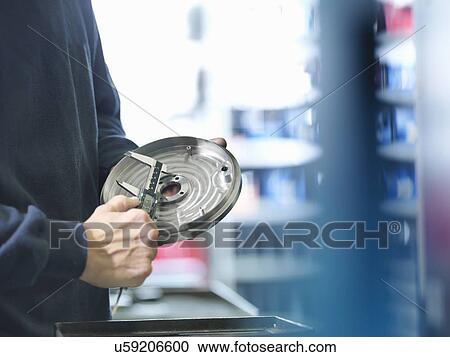 Stock Image - Engineer measuring metal part in factory, close up. Fotosearch
