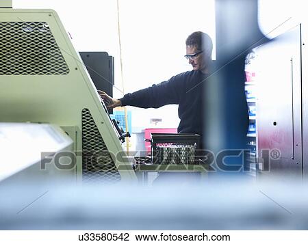 Stock Image - Engineer using lathe in factory. Fotosearch