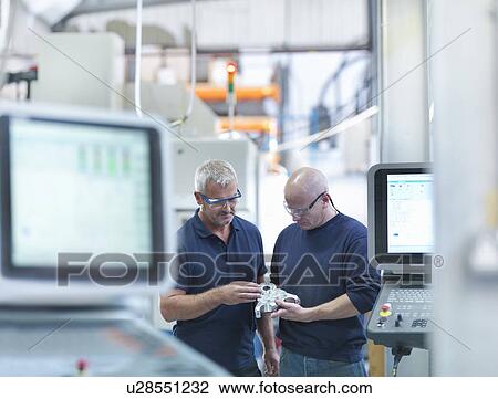 Stock Image - Engineers inspecting complex metal component in factory. Fotosearch