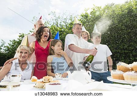 Stock Image - Family celebrating birthday, man opening champagne. Fotosearch
