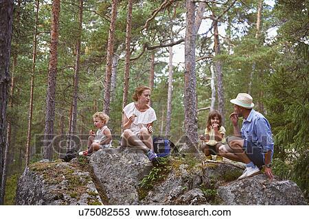 Stock Image - Family sitting on rocks in forest eating picnic. Fotosearch