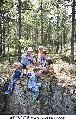 Family sitting on rocks in forest eating picnic View Large Photo Image Stock Photo - Family sitting on rocks in forest eating picnic. Fotosearch