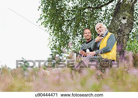Stock Image - Father and adult son drinking coffee from flask. Fotosearch
