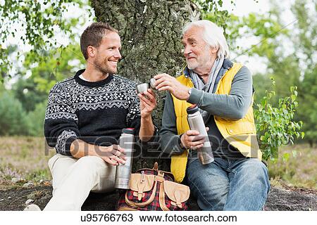 Stock Image - Father and adult son drinking coffee from flask. Fotosearch