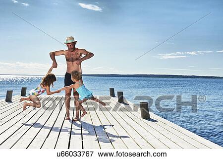 Stock Photo - Father and daughters playing on pier, Utvalnas, Gavle, Sweden. Fotosearch