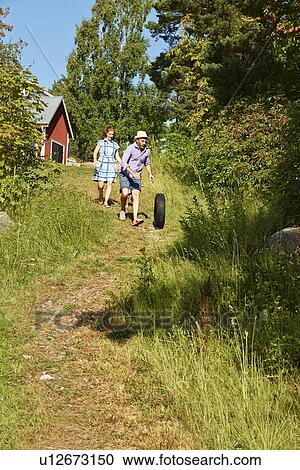 Stock Image - Female toddler and parents wheeling tyre, Utvalnas, Gavle, Sweden. Fotosearch