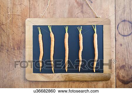 Stock Image - Five carrots on blackboard, still life. Fotosearch