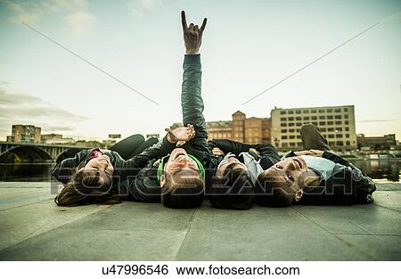 Stock Photograph - Four freinds lying on backs, one making rock and roll sign, Russia. Fotosearch