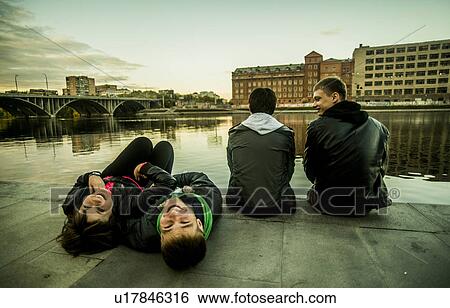 Stock Photograph - Four freinds sitting by river, two lying down, Russia. Fotosearch