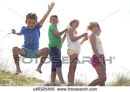 Stock Photography - Four friends on dunes, one boy jumping, Wales, UK. Fotosearch