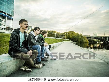Stock Photo - Four friends sitting on conrete wall, Russia. Fotosearch