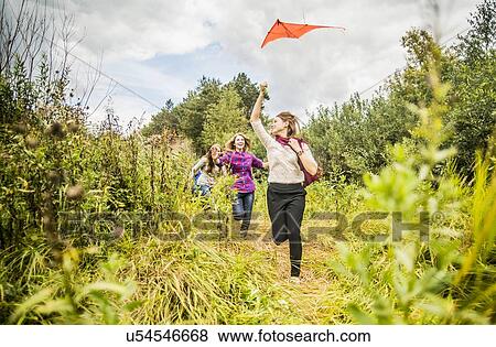 Stock Photo - Four young women running through scrubland with kite. Fotosearch