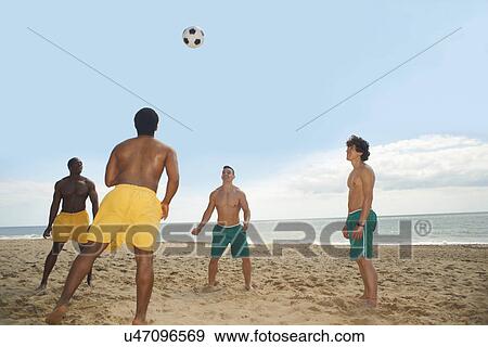 Stock Photo - Friends playing soccer on beach. Fotosearch