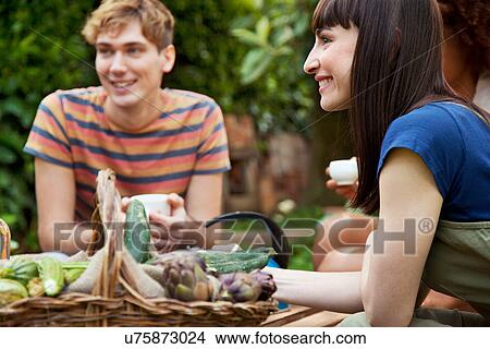 Picture - Friends sitting in garden with basket of fresh vegetables. Fotosearch