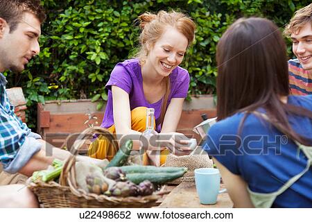Stock Image - Friends sitting in garden with basket of fresh vegetables. Fotosearch
