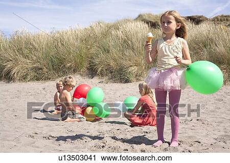 Girl holding balloon eating ice cream on beach, Wales, UK View Large Photo Image Stock Image - Girl holding balloon eating ice cream on beach, Wales, UK. Fotosearch
