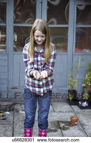 Stock Image - Girl in garden cupping seeds in hand. Fotosearch