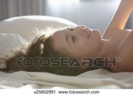 Stock Image - Girl lying on bed smiling. Fotosearch