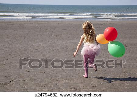 Stock Image - Girl on beach wearing tutu holding balloons, Wales, UK. Fotosearch