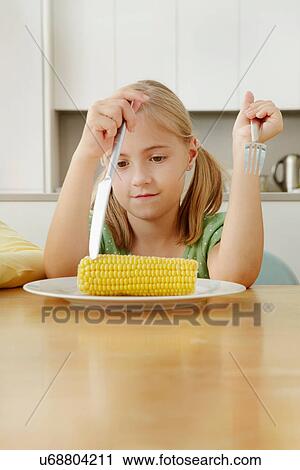 Stock Image - Girl poking at corn cob on plate. Fotosearch