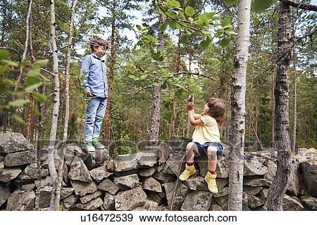 Girl sitting on wall taking photograph of boy View Large Photo Image Stock Photo - Girl sitting on wall taking photograph of boy. Fotosearch