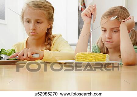 Stock Image - Girls poking vegetables on plate. Fotosearch