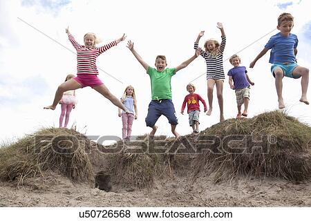 Stock Photo - Group of children jumping off sand dunes, Wales, UK. Fotosearch