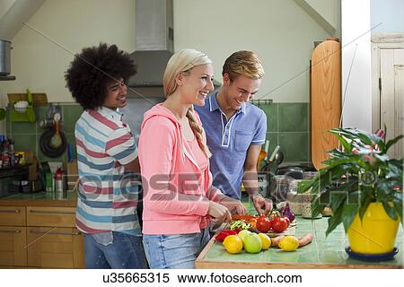 Stock Photography - Group of friends preparing vegetables in kitchen. Fotosearch